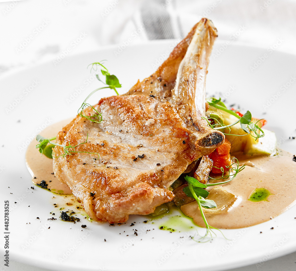 Roasted pork steak with vegetables garnish and sauce. Bone-in ribeye pork chops. Main course of pork in rustic style. Roasted pork steak with vegetables garnish and sauce. Bone-in ribeye pork chops. Main course of pork in rustic style.
