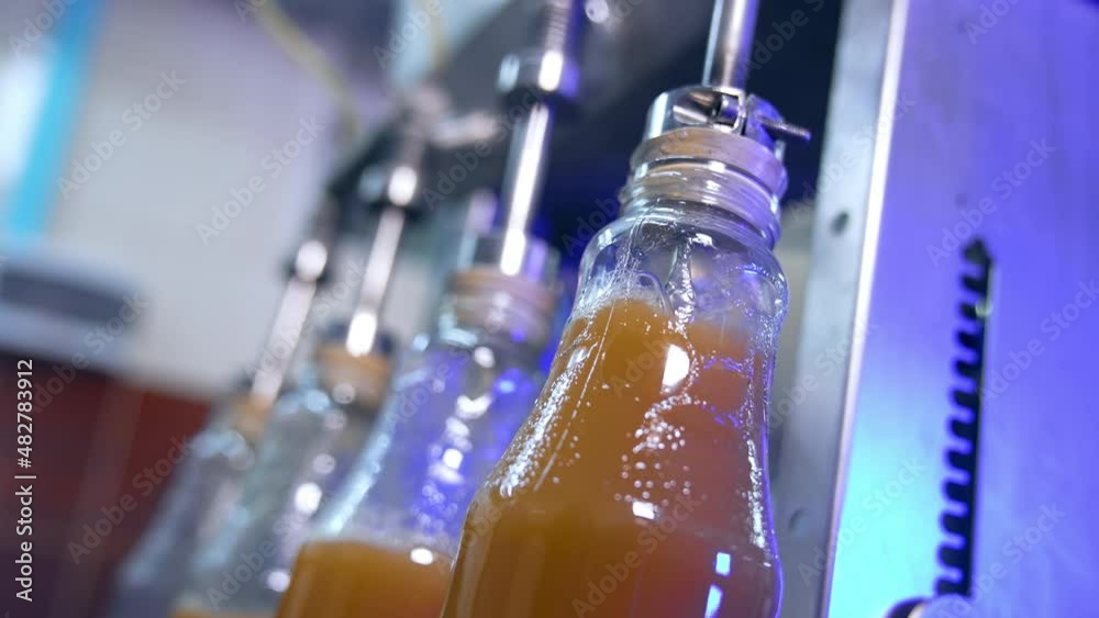 Few glass bottles being filled full with freshly-made juice. Automated technological process of juice manufacturing. Close up. Few glass bottles being filled full with freshly-made juice. Automated technological process of juice manufacturing. Close up.