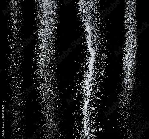 White refined sugar crystals falling down at black background.
