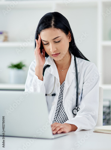 When the doctor needs a doctor. Shot of a young doctor looking stressed while using a laptop at her desk.