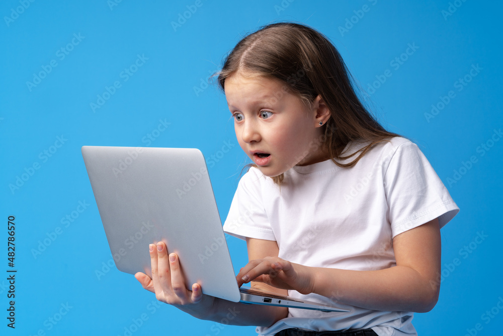 Portrait of a little girl holding laptop computer while standing against blue background Portrait of a little girl holding laptop computer while standing against blue background