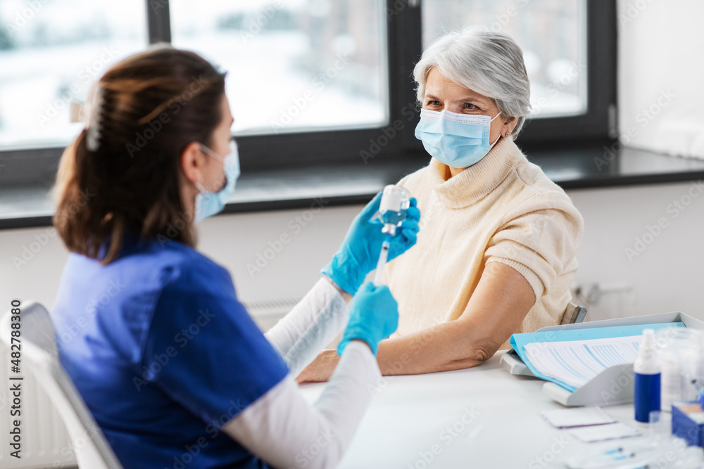 Obraz premium medicine, health and vaccination concept - doctor or nurse filling syringe with vaccine or drug and senior woman in mask at hospital