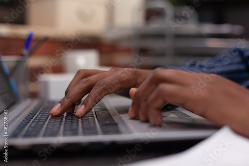 Closeup of african american hands typing business data on portable computer keyboard in startup brick wall office. Focus on startup employee using laptop for professional work or composing email.