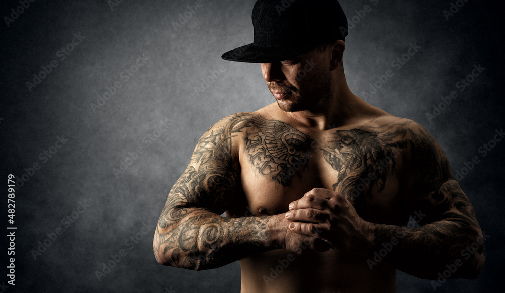 Bodybuilder with Tattoo. Strong Muscular Athletic Body Man. Power Athlete  in Hat over Dark Grunge Artistic Studio Background. Mysterious Handsome  Tattooed Men Portrait Stock Photo | Adobe Stock