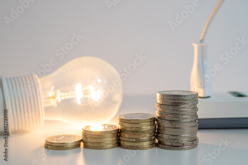 Light bulb on, with coins and a socket and plug next to it. Increase in electricity tariffs. 