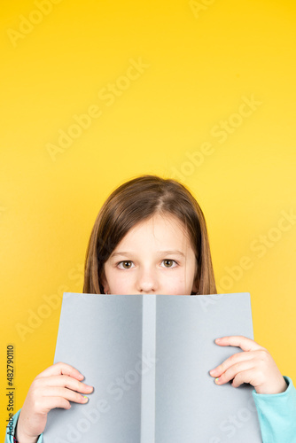 Child holding a book and looking to camera. Yellow copy space.