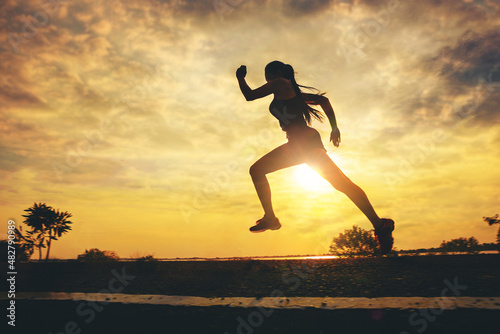 Silhouette of young woman running sprinting on road. Fit runner fitness runner during outdoor workout with sunset background. 