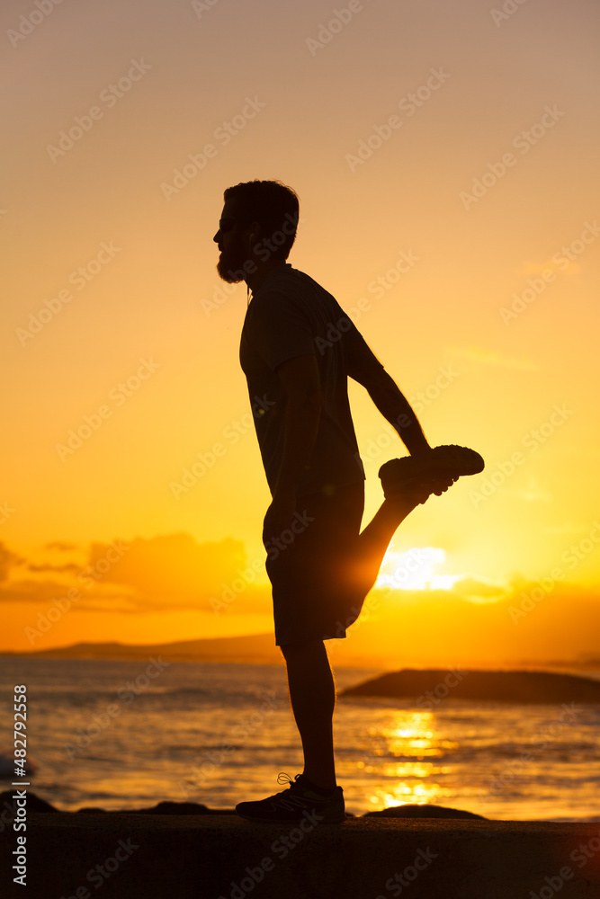 silhouette of a male runner stretching at sunset