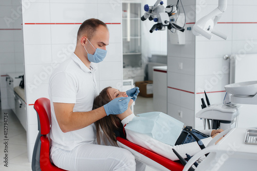 A young dentist specialist examines and treats the teeth of a beautiful woman in modern white dentistry. Dental prosthetics  treatment and teeth whitening. Modern dentistry.
