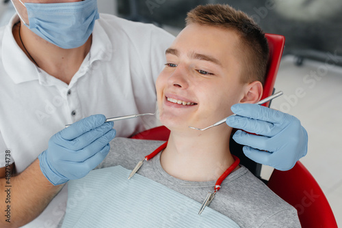 A young dentist examines and treats the teeth of a young man in modern white dentistry close-up. Dental prosthetics  treatment and teeth whitening. Modern dentistry. Prevention.