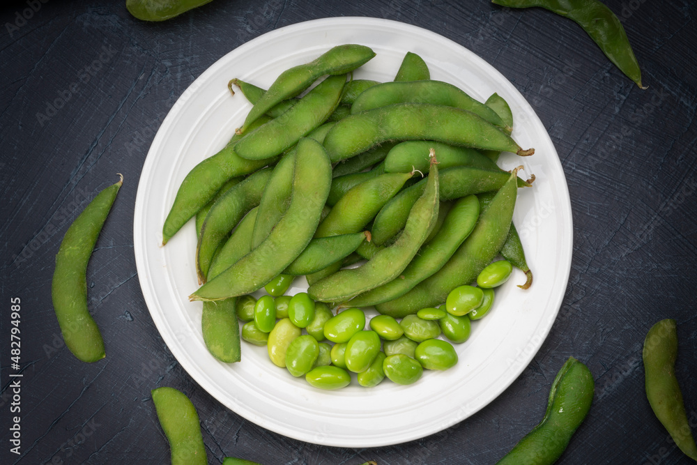 Green Edamame in white plate on wooden background, Steamed edamame sprinkled with sea salt on rustic black wooden table. Green Edamame in white plate on wooden background, Steamed edamame sprinkled with sea salt on rustic black wooden table.