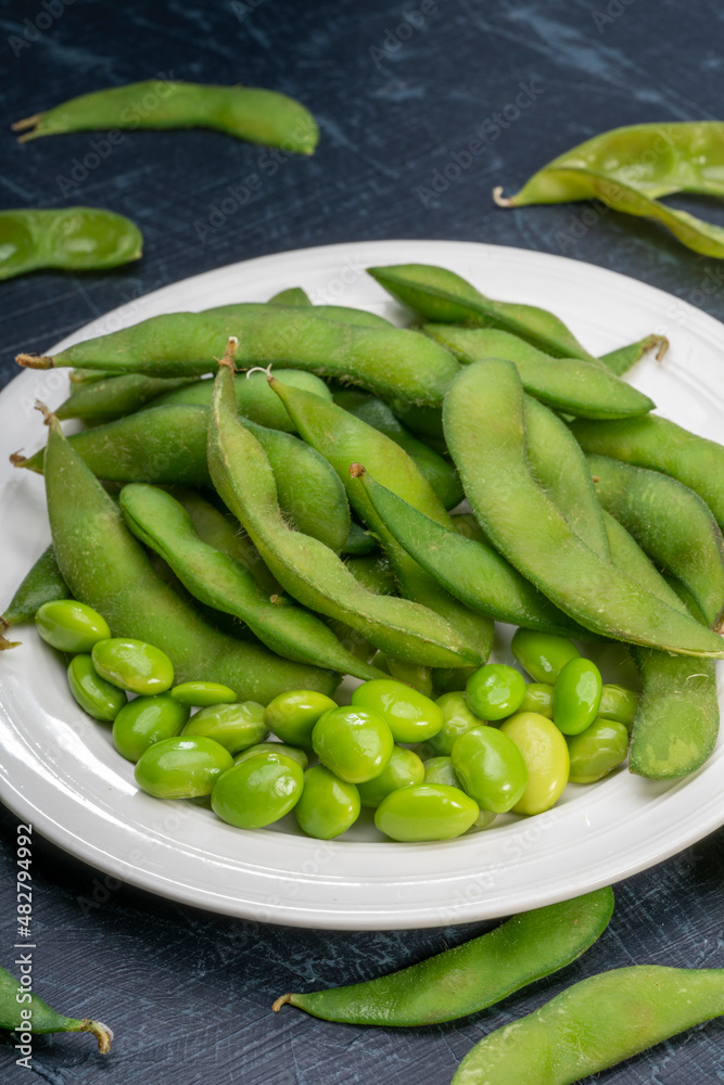 Green Edamame in white plate on wooden background, Steamed edamame sprinkled with sea salt on rustic black wooden table. Green Edamame in white plate on wooden background, Steamed edamame sprinkled with sea salt on rustic black wooden table.