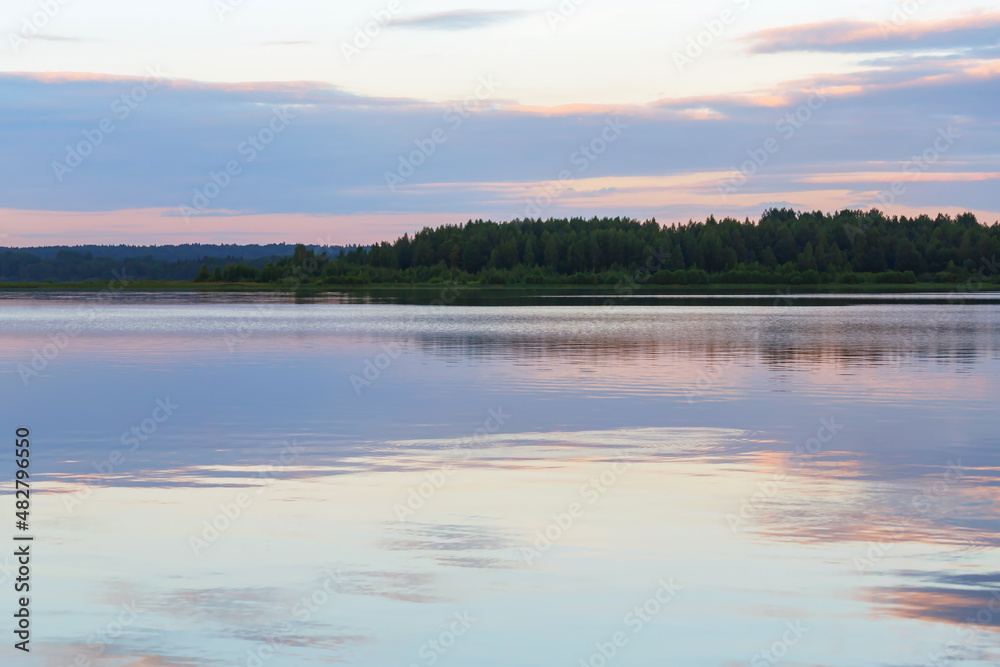 Scenic view on the calm river with forest on horizon. Last sun reflected in mirrow-like glossy water. Pastel colors, blue, pink and amethyst. Volga, Tver region, Russia