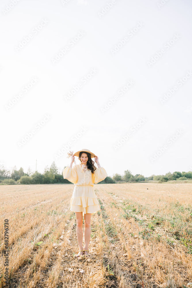 Young beautiful brunette on a summer day. girl in yellow dress. Large straw hat with a bouquet of wheat. Agricultural texture Young beautiful brunette on a summer day. girl in yellow dress. Large straw hat with a bouquet of wheat. Agricultural texture