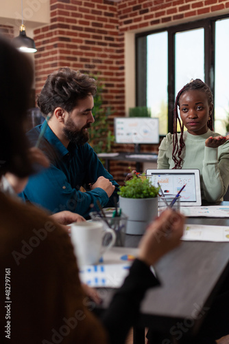 African american businesswoman showing marketing graphs to businesspeople explaining company turnover during business meeting in startup office. Diverse team working at financial project