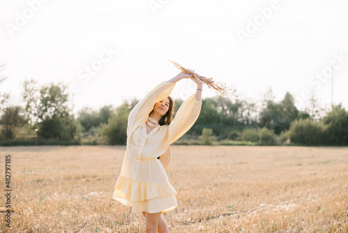 Portrait of a laughing Caucasian young brunette. girl in yellow summer dress and straw hat with a bouquet of wheat. sheared golden spike of wheat. Agricultural texture