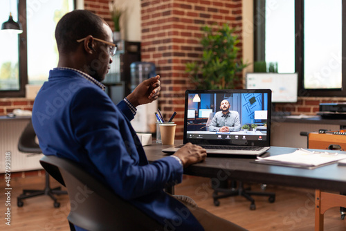 Company employee using video call conference on laptop to chat to man in startup office. Entrepreneur attending online teleconference meeting with person to discuss project and strategy.