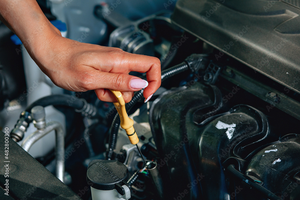girl's experienced hands are checking an oil in her broken car via an oil dipstick, close up girl's experienced hands are checking an oil in her broken car via an oil dipstick, close up