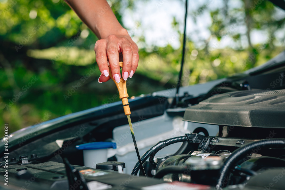 woman's hand is checking an oil in her car via an oil dipstick against the background of nature, close up woman's hand is checking an oil in her car via an oil dipstick against the background of nature, close up