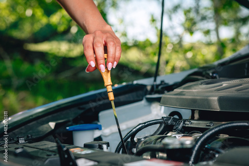 woman's hand is checking an oil in her car via an oil dipstick against the background of nature, close up