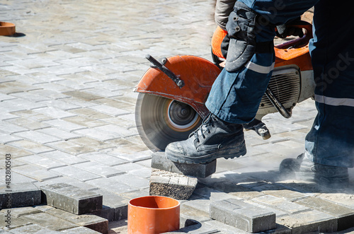 A worker cuts paving slabs with a gas cutter and a hand saw photo