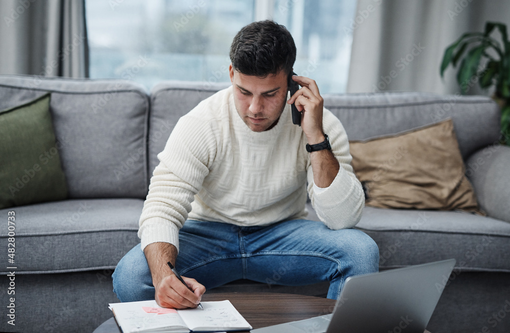 Part living space, part work space. Shot of a young man using a laptop and smartphone while writing in a notebook at home. Part living space, part work space. Shot of a young man using a laptop and smartphone while writing in a notebook at home.
