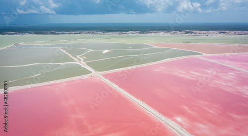Pink lake with white salt near the shore. In the background, a salt factory against a blue sky. Las Coloradas, Yucatan, Mexico