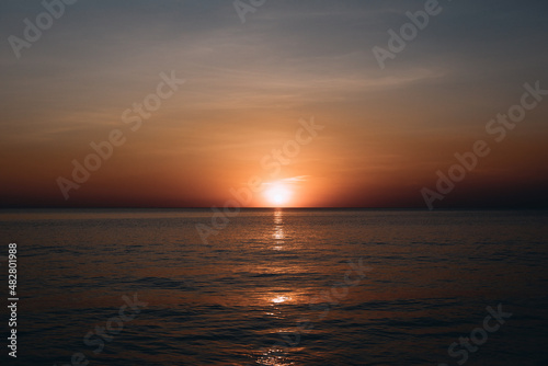 Breathtaking summer sunset view on the beach. Wonderful sunset landscape at the deep dark sea and orange sky above it and calm waves are flowing on it. © Semachkovsky 