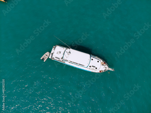 Aerial view of a white boat with a sharp bow and and a small boat next to it sailing across the sea