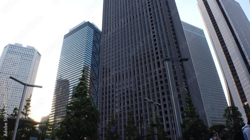 SHINJUKU, TOKYO, JAPAN - JULY 2021 : Exterior of tall office buildings in sunset time. Wide low angle time lapse shot, dusk to night. Japanese urban metropolis and business concept shot. SHINJUKU, TOKYO, JAPAN - JULY 2021 : Exterior of tall office buildings in sunset time. Wide low angle time lapse shot, dusk to night. Japanese urban metropolis and business concept shot.