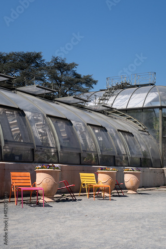 détail d'une serre en verre avec des chaises colorées et des pots de fleurs