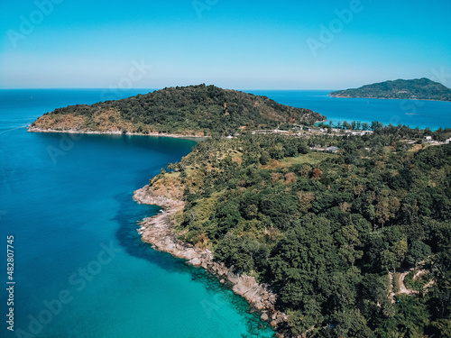 Top view of a coast of a huge uninhabited island covered with dense wild forest, around which the blue sea