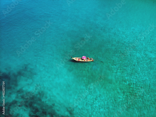 Fototapeta Naklejka Na Ścianę i Meble -  A lonely boat is floating peacefully in the middle of a vast blue ocean, aerial view