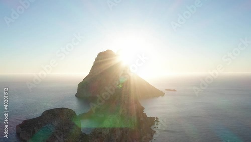 Aerial view of sunset coming from behind Es Vedra Ibiza with sunstar. Showing ocean and clear skies. Panning down. photo