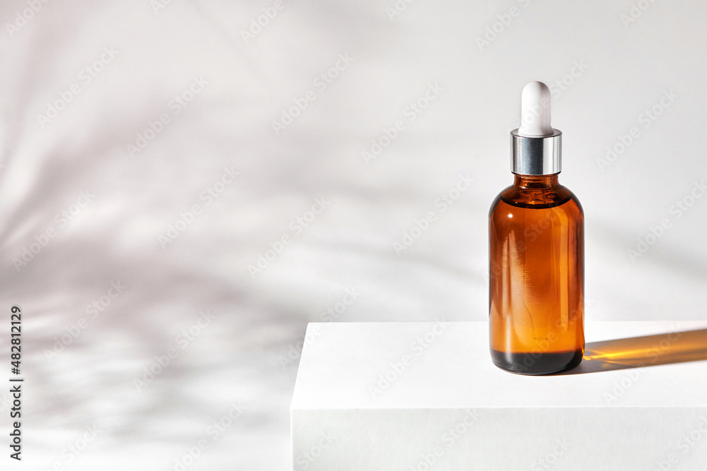 Essential oil on a gray background with shadows. Cosmetic medical beauty product in brown glass bottle with a pipette for aromatherapy, alternative medicine.