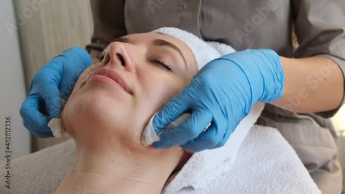 A young beautiful girl lies on the table at the beautician and receives facial cleansing procedures, makeup removal with white wipes  