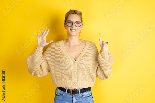 Young beautiful woman wearing casual sweater over isolated yellow background showing and pointing up with fingers number six while smiling confident and happy