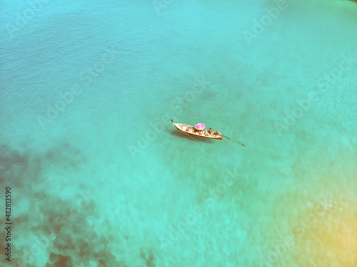 Aerial view of the wooden Thai boat with a pink parasol sailing the immensely clear sea, tourism; paradise concept.