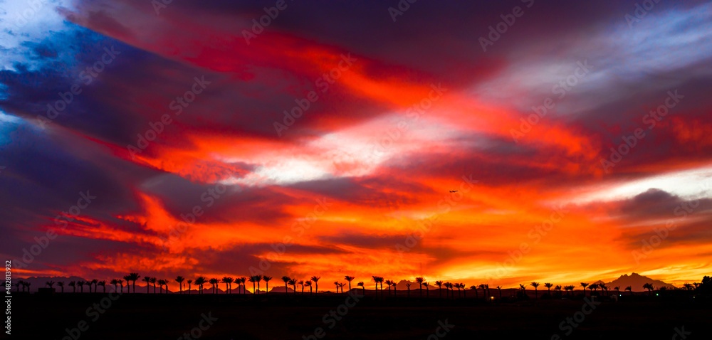 very beautiful orange, red, yellow and purple colors of the sunset sky with silhouettes of mountains and palms in egypt, sahl hashish