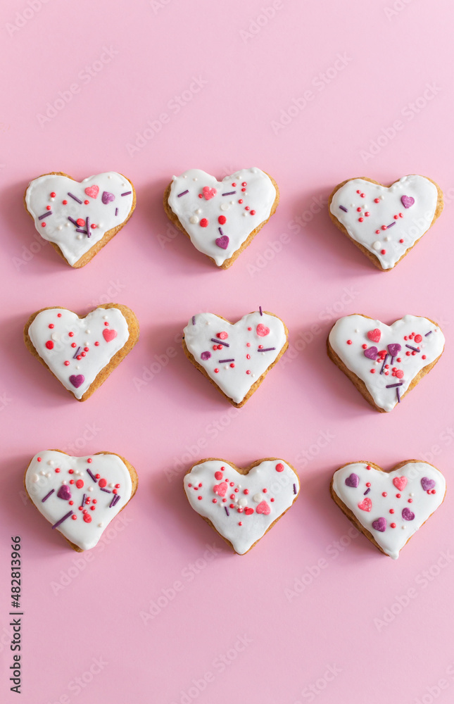 Gingerbread covered with white icing and sprinkling on a pink background. The concept of celebrating Valentine's Day. Vertical orientation. Top view. Gingerbread covered with white icing and sprinkling on a pink background. The concept of celebrating Valentine's Day. Vertical orientation. Top view.