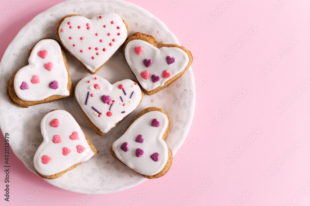 Gingerbread covered with white icing and sprinkling on a white saucer on a pink background. The concept of celebrating Valentine's Day. Horizontal orientation. copy space. Top view. Gingerbread covered with white icing and sprinkling on a white saucer on a pink background. The concept of celebrating Valentine's Day. Horizontal orientation. copy space. Top view.