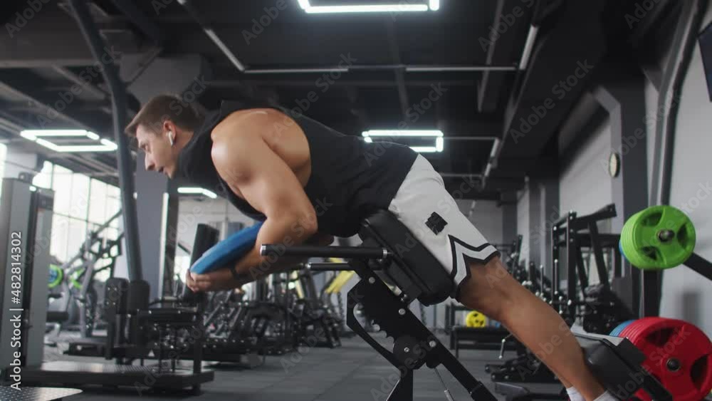 Man with headphones trains back muscles and abs in gym, side view. Man of athletic build trains lifting heavy weight. Concept bodybuilding Man with headphones trains back muscles and abs in gym, side view. Man of athletic build trains lifting heavy weight. Concept bodybuilding