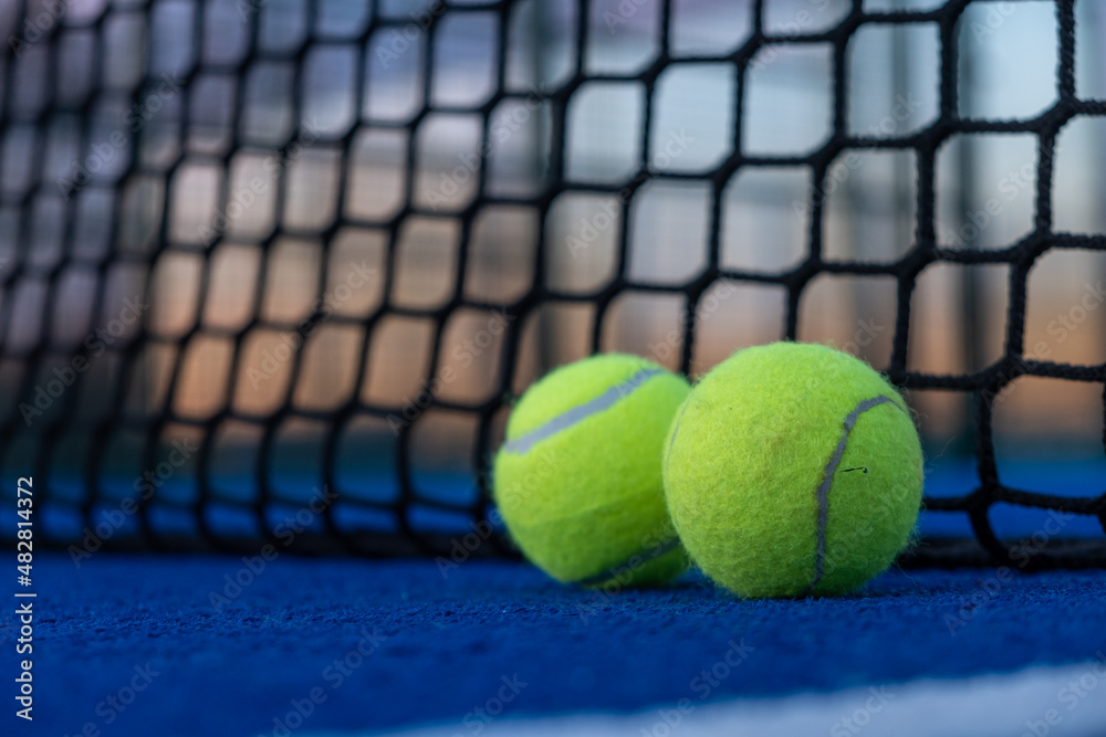 Selective focus. two paddle tennis balls by the net of a blue paddle tennis court at sunset