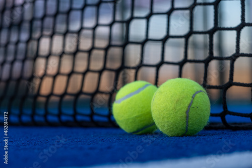 Selective focus. two paddle tennis balls by the net of a blue paddle tennis court at sunset © Vic
