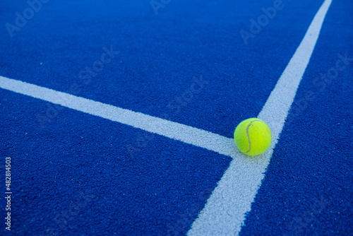 Paddle tennis ball on the line of a blue paddle tennis court. © Vic