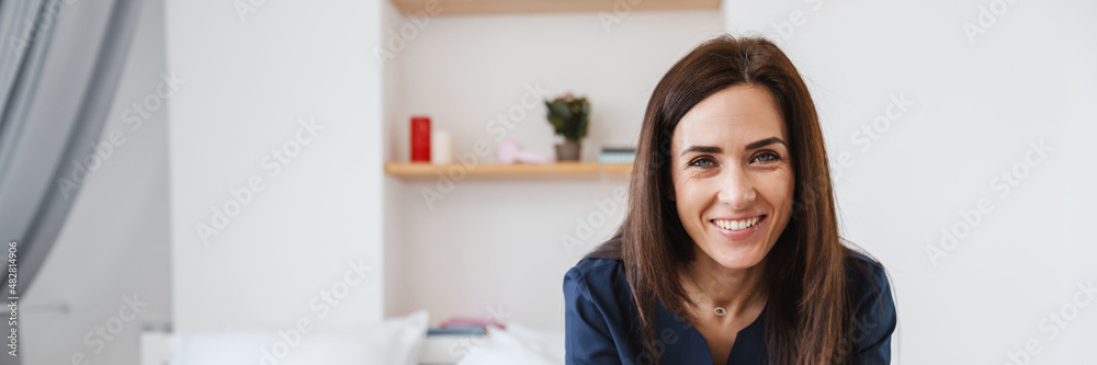 The smiling woman in medical uniform sitting on bed and laughing at camera in the room The smiling woman in medical uniform sitting on bed and laughing at camera in the room