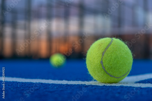 Selective focus. Paddle tennis ball in the foreground on a blue paddle tennis court at sunset.