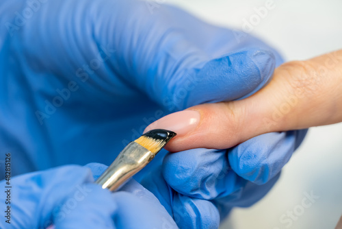 Close-up of a manicure master in blue gloves draws a black jacket on the nails of a client with a brush. Professional manicure with gel polish and pattern