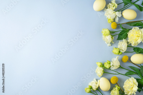 Coloured yellow eggs and various white flowers on light blue background. Festive Easter layout in pastel colors. Spring holiday composition. Flowers and chicken eggs flat lay. Copy space, top view.