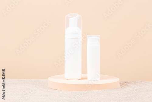 Canvas Print Two white blank plastic packaging cosmetic pump bottles for mousse foam cream and lotion stand on round podium, beach sand and beige background